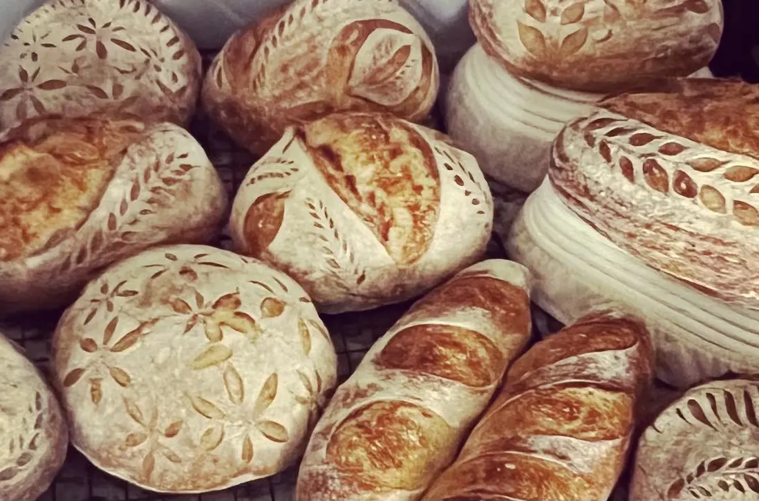 A tray of freshly baked sourdough boules and baguettes cooling on a rack
