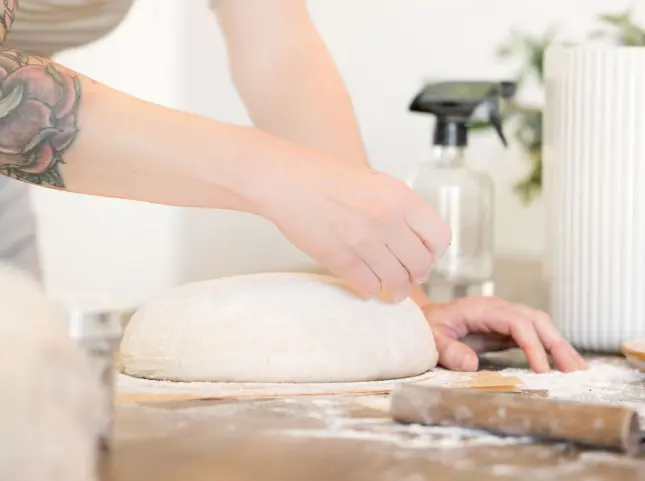 Hands carefully scoring a round of proofed sourdough dough before baking